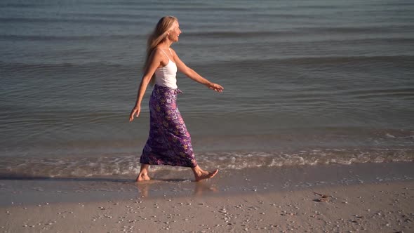 Slow motion of mature woman in sarong walking on a beach and throwing her arms out to the side celeb alt