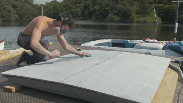 Young shirtless man wiping down plywood engine cover with acetone before painting alt