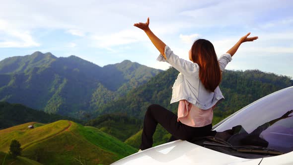Young woman traveler sitting on a car watching a beautiful mountain view
