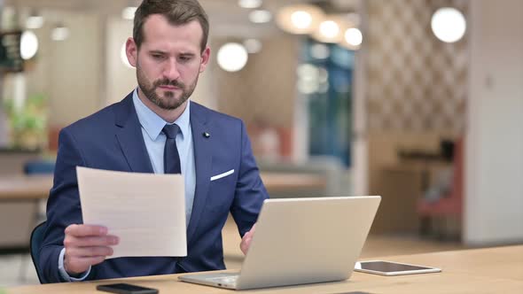 Serious Businessman Working on Laptop with Documents in Office alt