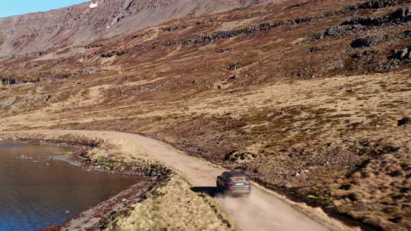 Car On  Dirt Track By Fjord Towards Waterfall On Mountain alt