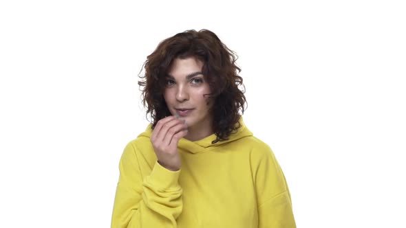 Shy and Coquettish Attractive Young Woman in Yellow Hipster Hoodie Blowing Wind Kiss and Glancing alt