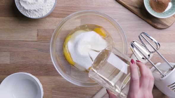 Female Hands Pour Oil into Cake Mix - Top Down Shot alt