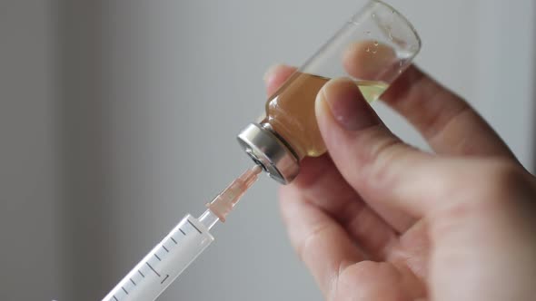 Female hands inject the solution into a vial of vaccine with a syringe