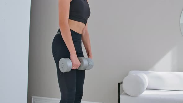 A Young Athletic Woman in a Bright Apartment Performs a Deadlift with Dumbbells at Home Making Leans alt
