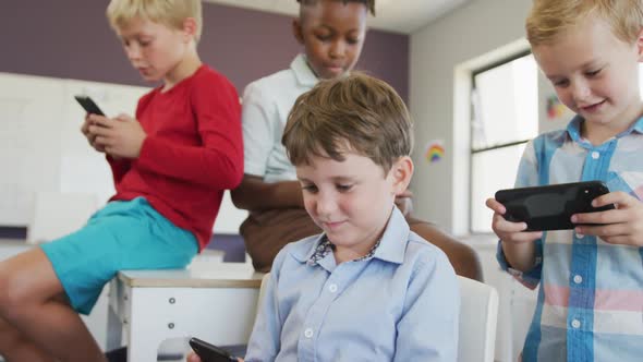 Video of diverse boys sitting at school desks and playing games on smartphones alt
