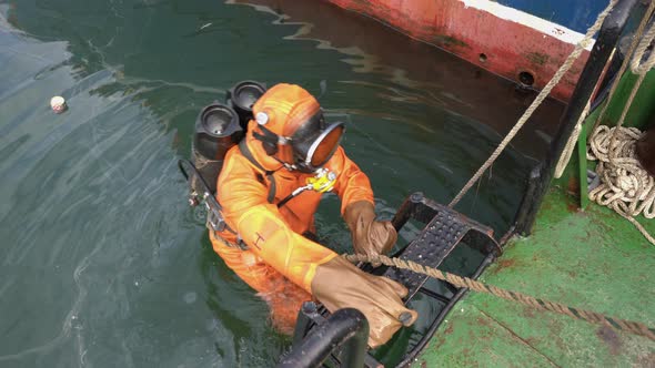 Frogman in Orange Equipment for Diving Climbs Ladder Out of Water on Boat