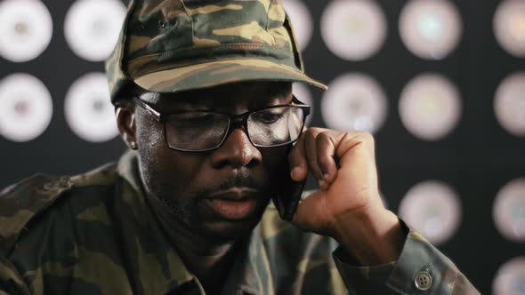 Portrait of Black Man in Military Clothes Speaks on Phone Sitting at Desktop