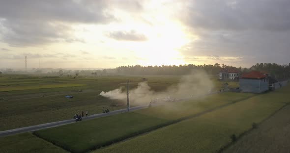 Aerial drone view of farming fields and a road with burning smoke at sunset. alt