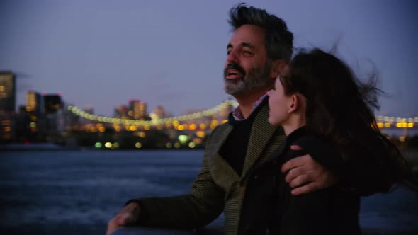 Couple in New York City standing on pier at night with city skyline in background