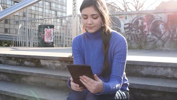 Young woman outdoor backlight using tablet hand hold looking camera smiling alt