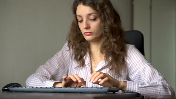 Young Female Office Manager in White Shirt and Curly Hair is Sitting at the Table and Typing Using alt