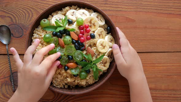 Wholegrain Oatmeal porridge with fresh berries, fruits, nuts, mint leaves in child hands. alt
