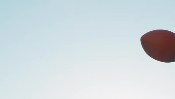 Slow motion close-up of a football as it arcs through the sky. A lens flare can be seen half way thr alt