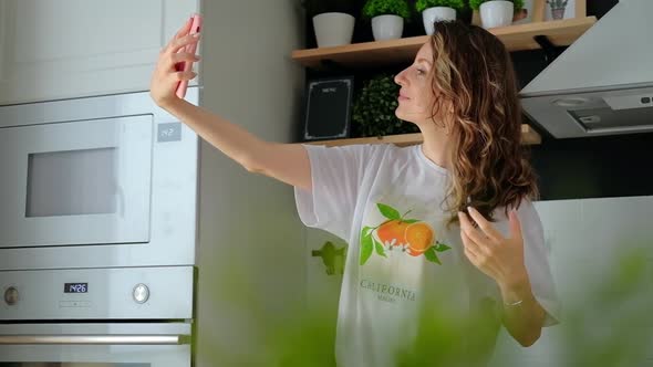 Young pretty woman taking selfie sitting at her kitchen at home. Smiling woman taking selfie. 