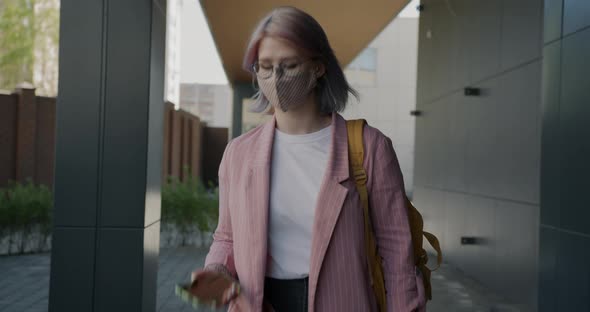 Dolly Shot of Joyful Student Wearing Face Mask Talking on Mobile Phone Walking Outdoors alt