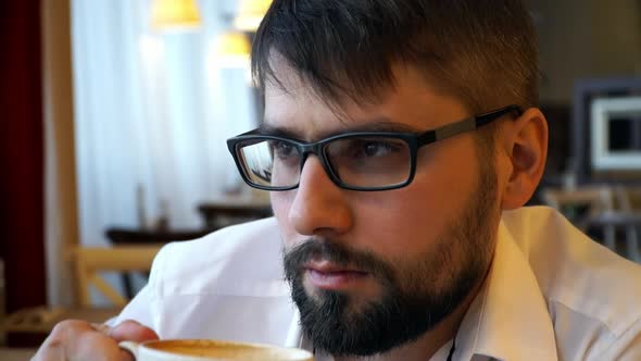 Close Up of Man Sits in Cafe and Drinks Coffee From Cup in Coffee House