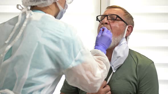 Lab Technician in a Protective Suit Takes a Swab From an Elderly Patient for Coronavirus. alt