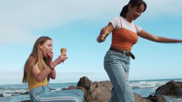Side view of a Caucasian and a mixed race girl eating ice cream seaside alt