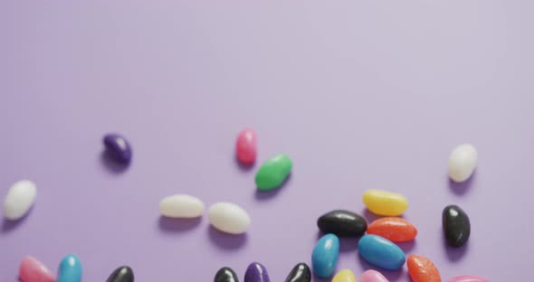 Video of overhead view of multi coloured sweets with copy space over purple background alt