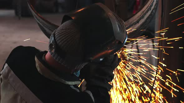 The Welder Processes the Weld with a Grinding Machine and Sparks Fly