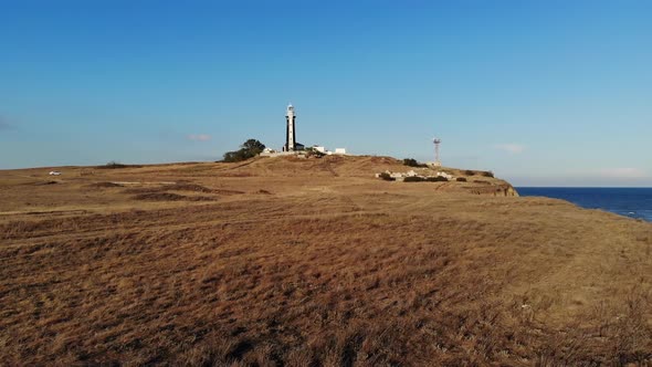Aerial View of an Unknown Lighthouse with Black and White Edges on the Peninsula's Promontory alt