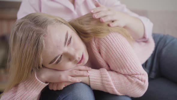 Close-up Portrait of Crying Caucasian Girl Lying on Mother's Knees and Talking. Teenage Daughter alt