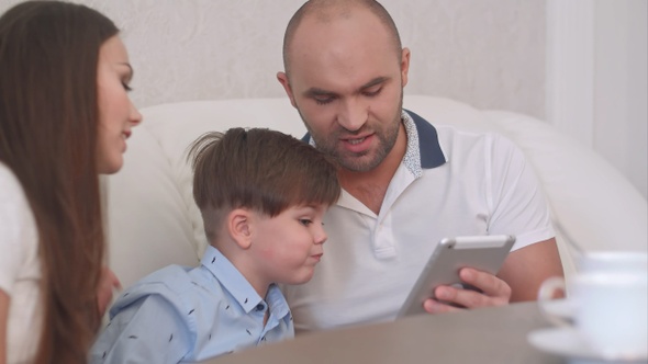Young father showing something on the tablet to his wife and sons