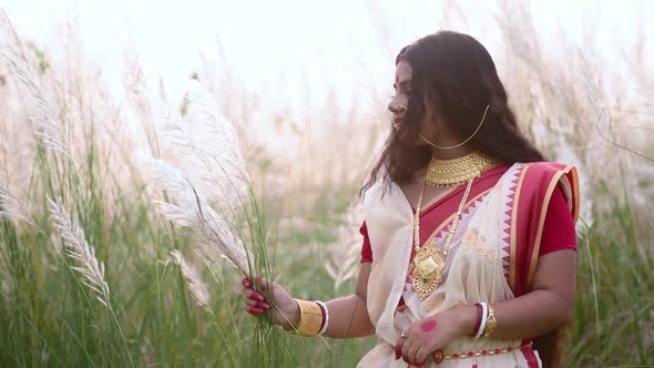 A happy and beautiful Indian bengali woman plays with the long white grass Kaash phool in a field we alt