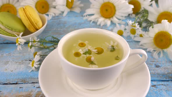 Composition with chamomile flowers, herbal tea and macaroons on vintage light blue wooden tabletop. alt