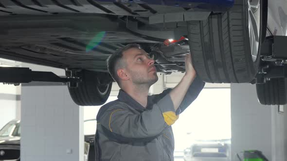 Sliding Shot of Auto Mechanic Checking SUV Suspension of a Lifted Car