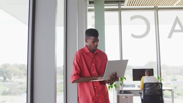 African american creative businessman standing with laptop in modern interiors alt