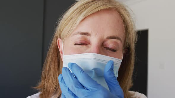 Caucasian senior female doctor wearing surgical gloves adjusting face mask alt