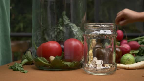 woman prepares tomatoes for canning in jar next to a window on background