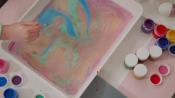 Little Child Draws Flower on Oily Water Surface with Paints alt