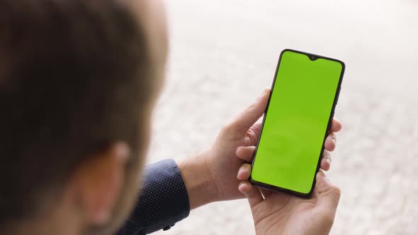 A Man Looks at a Smartphone (Vertical) with Green Screen  Closeup From Behind the Shoulder