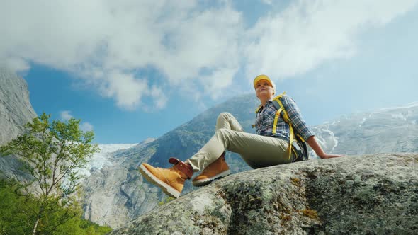 A Woman Is Sitting on a Big Stone Surrounded By the Picturesque Nature of Norway  alt