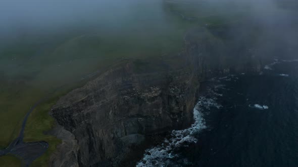 Aerial Shot of High Vertical Rock Walls Above Rippled Sea Surface After Sunset alt