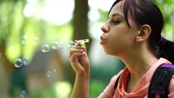 Young Woman Blowing Bubbles on Nature. Happy Young Brunette Woman Strolls in the Park and Makes Soap alt