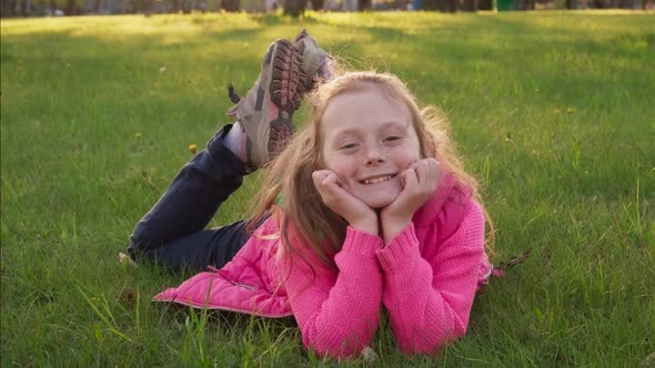 Joyful Carefree Little Girl Lying on Grass and Smiling in Summer Park alt