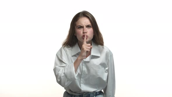 Attractive Young Brunette in White Collar Shirt Telling to Shut Up Showing Hush Sign and Frowning alt