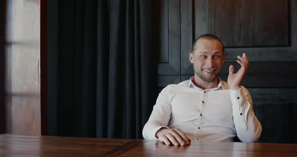 Exasperated Man Sitting at an Indoor Table Shaking His Head and Gesturing with His Hands Showing alt