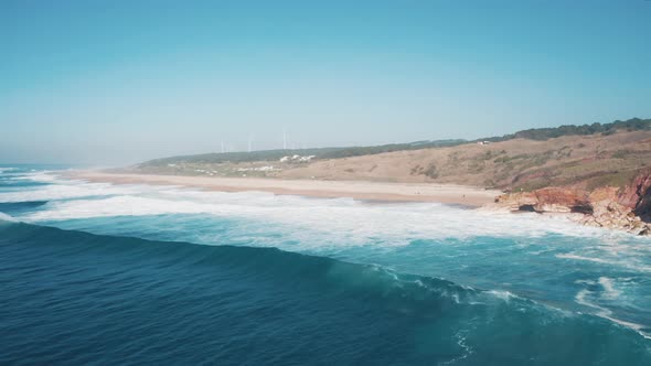 Aerial; drone view of deserted Nazare norte beach with wind turbine; blue stormy water of Atlantic