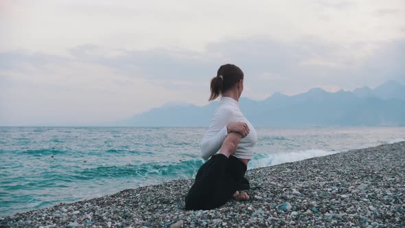 A Woman in White Sweater Stretching Her Leg on the Pebble Beach alt