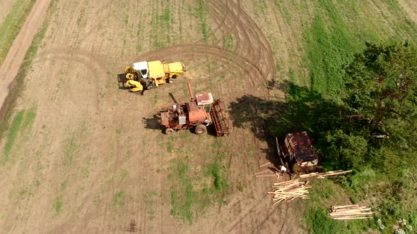 Harvesters Stand on Wide Field Between Tree and Road Aerial