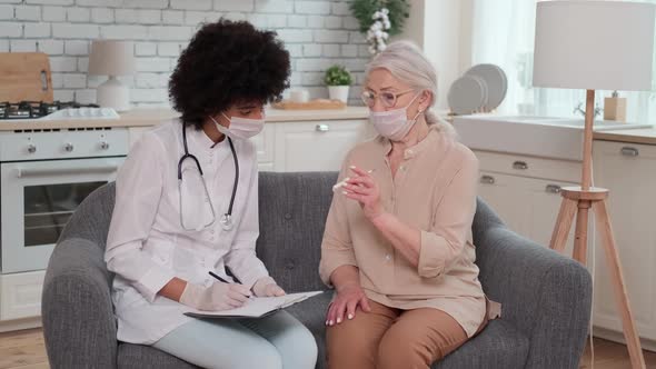 Afro American Woman Doctor in Mask Looks at Body Temperature Senor Woman Looking at Thermometer alt