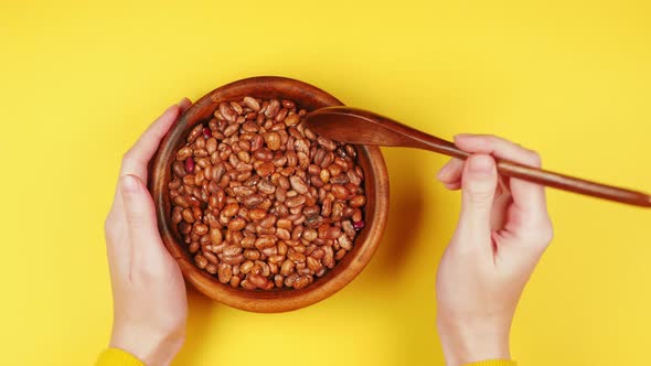 Young girl's hands are holding a wooden eco friendly plate with raw protein beans and stirring with