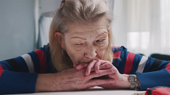 Desperate Old Woman Pensioner Looking at Small Amount of Coins on the Table alt