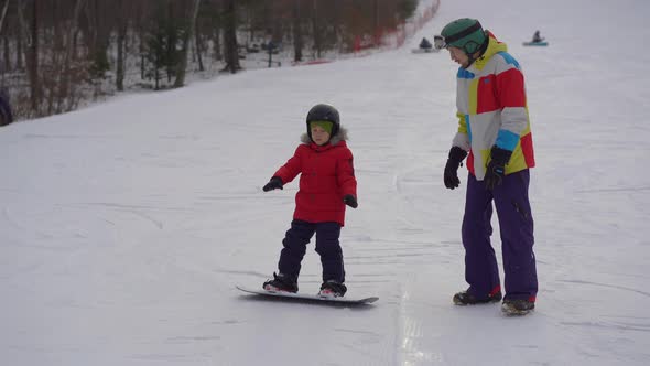 Young Man Snowboard Instructor Tiches Little Boy How To Ride a Snowboard. Winter Activities Concept alt