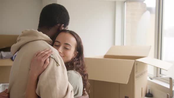 Young Couple With Keys To New Home Hugging As They Unpack Removal Boxes In Kitchen Together